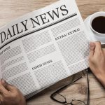 Hands with newspaper and cup of coffee on table